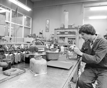 883633 Afbeelding van een monteur van de R.E.M.U. tijdens werkzaamheden aan een gasmeter in de werkplaats van de ...